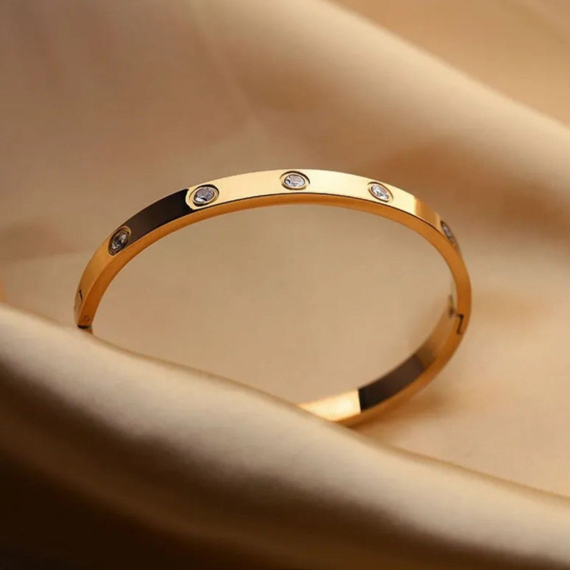 Gold bracelet with embedded stones on a beige fabric background